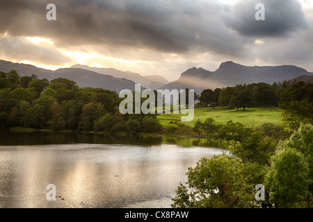Sun setting over Langdale Pikes with Loughrigg Tarn in foreground Stock Photo