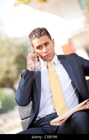 Businessman sited in a bench calling at the cellular and reading his ...