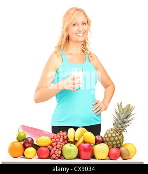 Woman holding a glass of milk with pile of fruits on a table, isolated on white background Stock Photo