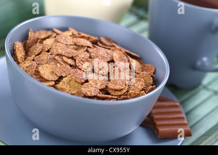 Bowl of chocolate corn flakes cereal with cup of coffee/tea and a jug of milk in the back Stock Photo