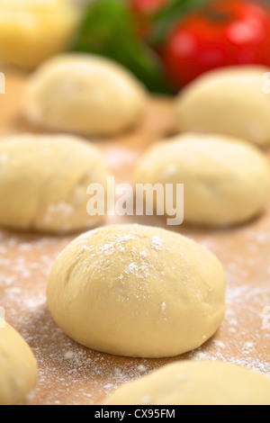 Small balls of fresh homemade pizza dough on floured wooden board with pizza ingredients (tomato, basil, grated cheese) Stock Photo