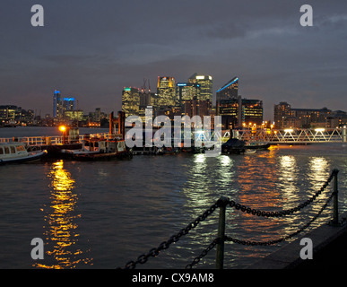 Night view of Canary Wharf skyscrapers showing the River Thames and Thames Clippers pier in foreground. Stock Photo