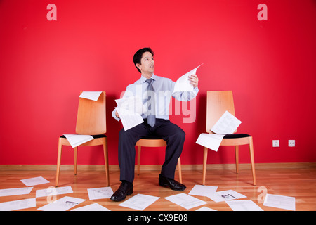 Businessman reading a document in a messy office full of papers on the floor Stock Photo