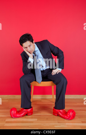 Businessman sited next to a red wall with clown shoes Stock Photo