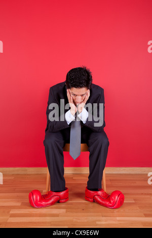 Businessman sited next to a red wall with clown shoes Stock Photo