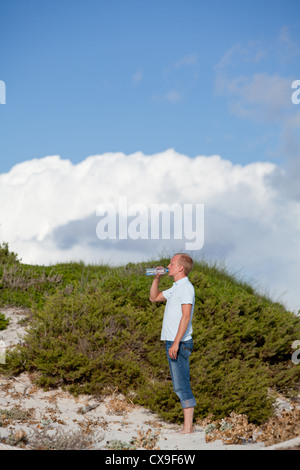 young man ist drinking water summertime dune beach sky background Stock Photo