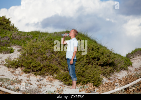 young man ist drinking water summertime dune beach sky background Stock Photo