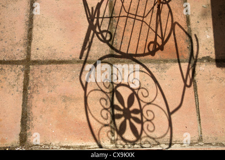 Shadow of metal patio chair on patio slabs. Stock Photo