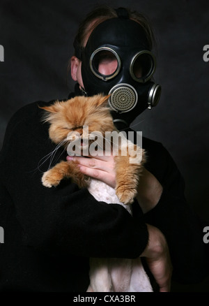 The man in a gas mask holds a shouting red cat Stock Photo