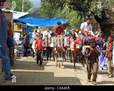 People on horseback and on foot making the climb to the Vaishno Devi Shrine in India. There are shops along the path. Stock Photo