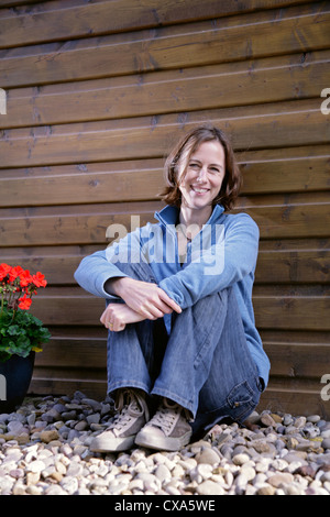 Happy young woman leaning against a wooden wall Stock Photo