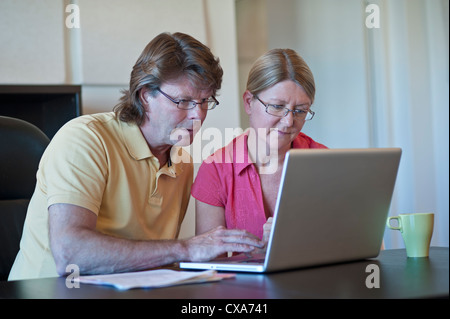 Mature couple at home using their laptop computer together, in light contemporary living room office. Stock Photo