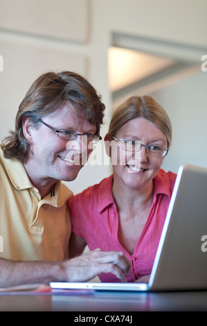 Attractive couple at home using their laptop computer together, in light contemporary living room office. Stock Photo