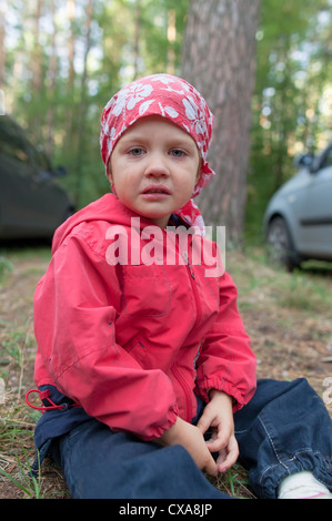 Crying little girl sitting on the ground in forest Stock Photo