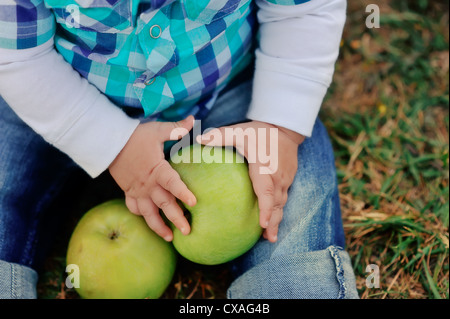 baby sitting in jeans and holding green apples Stock Photo