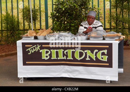 Woman texting on her mobile phone whilst selling Biltong at a roadside stall. Amanzimtoti, KwaZulu-Natal, South Africa. Stock Photo