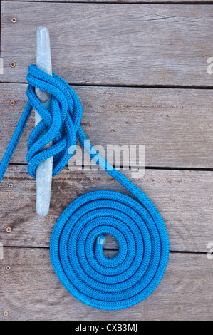 Blue rope coiled on a wooden dock and tied to a metal dock cleat. Cleats are used for securing docks and lines from boats Stock Photo