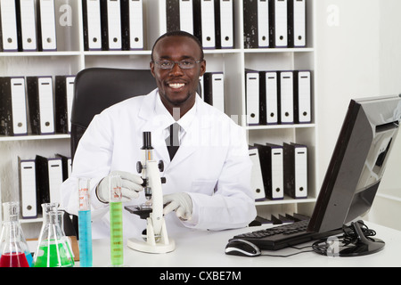 african american medical scientist wearing lab coat with microscope and test tubes in laboratory Stock Photo
