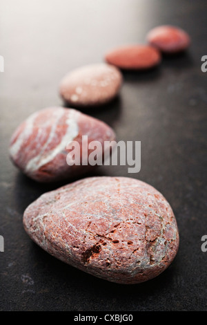 Curving line of red and grey pebbles arranged on dark textured background. Stock Photo