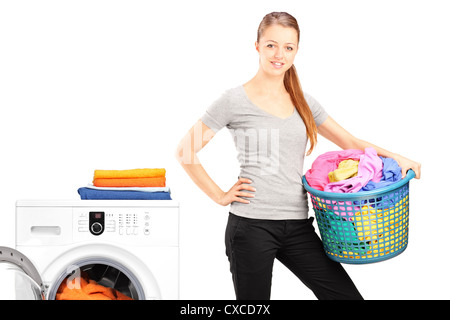 A smiling woman holding a laundry basket next to a washing machine isolated on white background Stock Photo