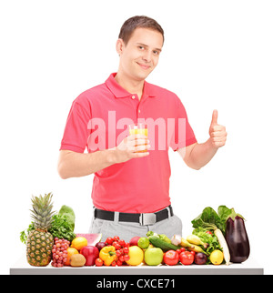Casual guy holding a juice and giving thumb up with pile of food on a table, isolated on white background Stock Photo