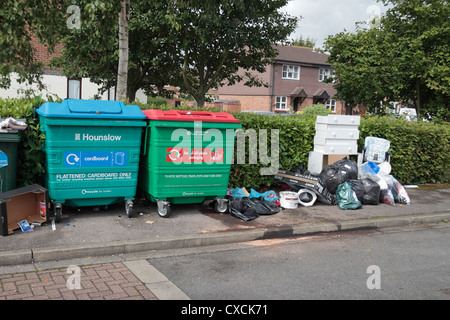 Illegal fly tipping beside plastics and cardboard recycling containers on a small flat development in Hounslow Middx, UK. Stock Photo