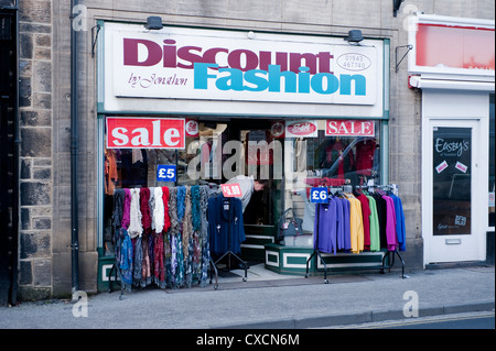 Discount Fashion shop selling clothing bargains (sale signs, clothes on hanging rails outside & woman looking in window) - Otley, Yorkshire, England. Stock Photo