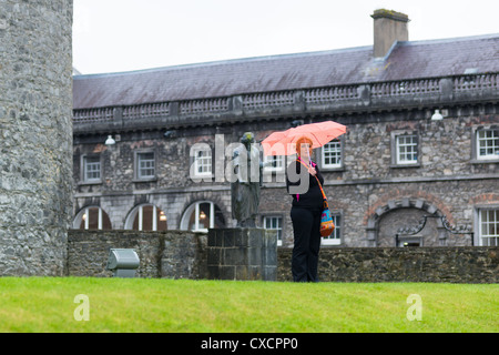 Woman stands in the rain at Kilkenney Castle with the design centre to the rear, Republic of Ireland. Stock Photo