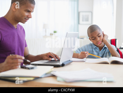 Father working and son doing homework Stock Photo