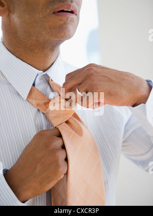 Mixed race man tying necktie Stock Photo