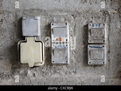It's a photo of 4 switches and 2 electrical outlets or power outlets that are on a wall make of concrete and agglo or chipboard Stock Photo