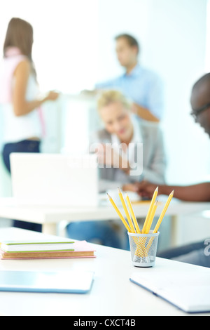 Close-up of several pencils in plastic glass on background of group of students working Stock Photo