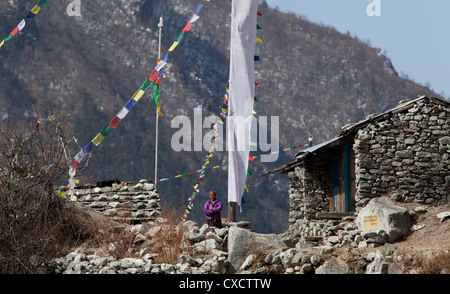 Nepali woman standing next to her traditional stone house surrounded by colourful prayerflags, Langtang village, Nepal Stock Photo