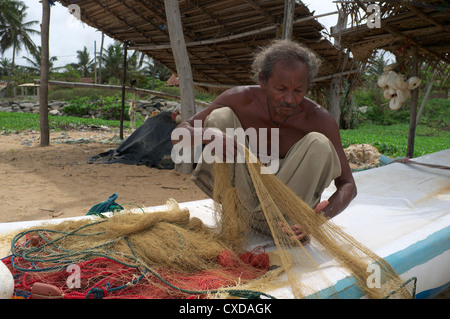 Sri Lanka fisherman repairing his fishing net while sitting on his small boat, Waikkal, Sri Lanka Stock Photo