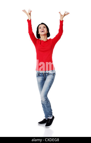 Smiling young woman is holding something abstract above her head. Happy girl with raised hands. Isolated on white background.  Stock Photo