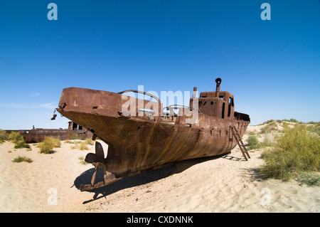 Rusty boats lay still on the dry desert sea bed of the dried Aral sea. Stock Photo