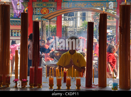 lighting candles and incense for good luck during Chinese New Year at Wat Mangkon Kamalawat in Bangkok's Chinatown Stock Photo