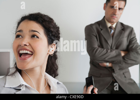 Woman distractedly listening to MP3 player at work, angry boss in ...