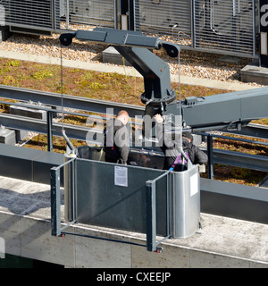 Roof mounted crane and tracks on roof of office building with two men in maintenance cradle checking equipment Stock Photo
