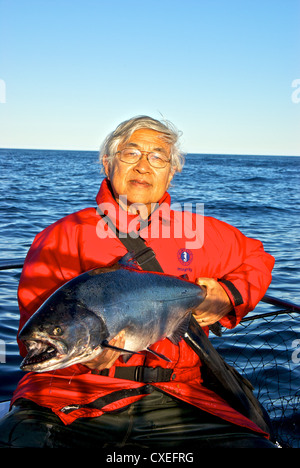 Male Asian angler holding big chinook salmon fishing Pacific Ocean offshore Ucluelet BC Stock Photo