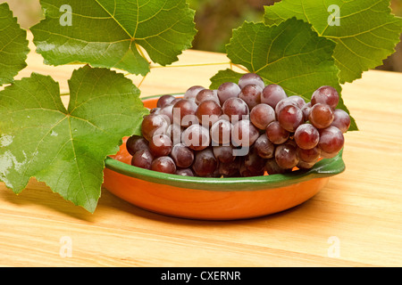 Red table grapes and leaves on wooden table Stock Photo