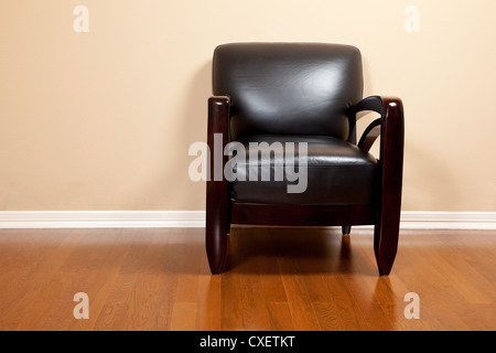 A black leather chair on a wooden floor against a wall with copy space Stock Photo