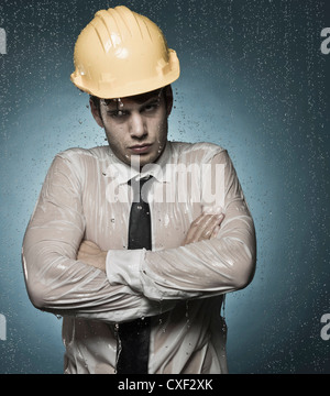 Caucasian businessman in hard-hat standing in rain Stock Photo