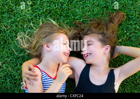 Blond and brunette sisters kid girls smiling lying on garden grass Stock Photo