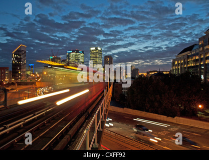 Night view of DLR train at East India DLR station showing Canary Wharf in background, London, England, United Kingdom Stock Photo