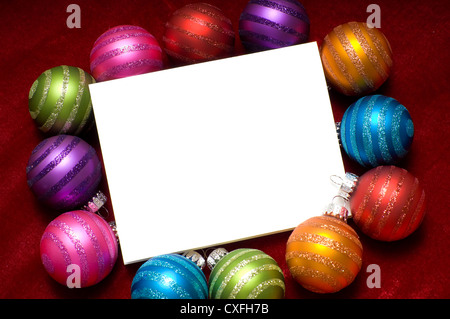 A blank notecard surrounded by multicolored Christmas ornaments on a red background Stock Photo
