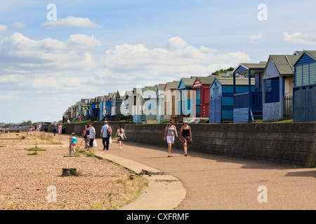 People walking on Whitstable seafront promenade beside beach huts on north Kent coast Thames estuary. Tankerton Whitstable Kent England UK Stock Photo