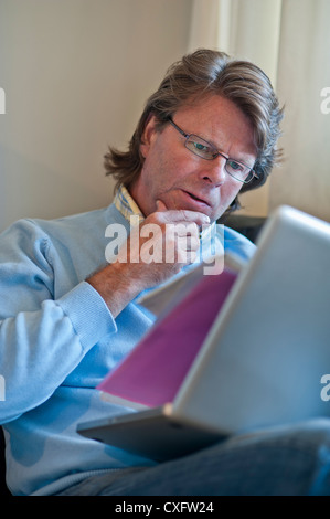 Mature man at home checking business paperwork using his laptop computer Stock Photo