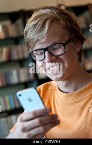 Attractive happy studious  teenage schoolboy in library using his Apple iPhone 4s smartphone Stock Photo