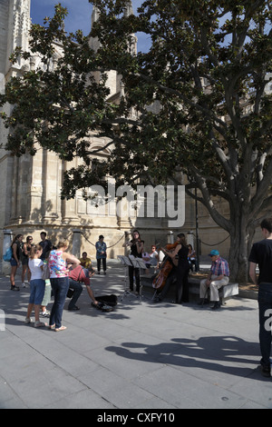 Person giving money to young classical musicians busking in the Plaza Virgen de los Reyes by Seville Cathedral Spain Stock Photo
